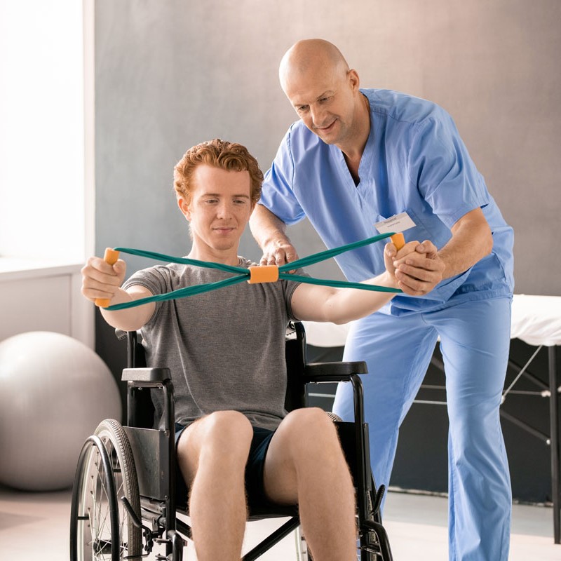 Mature clinician in blue uniform supporting hand of young patient in wheelchair Mature clinician in blue uniform supporting hand of young patient in wheelchair