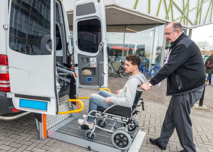 Taxi Driver Assisting Man On Wheelchair To Board Van
